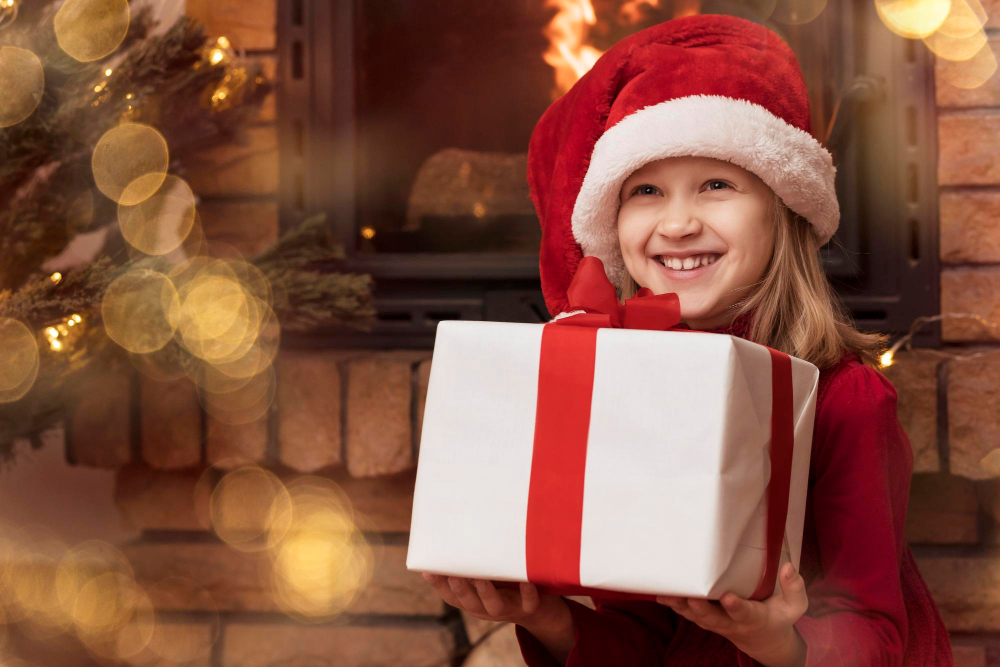 christmas child girl santa hat with big gift box red present near christmas tree fireplace
